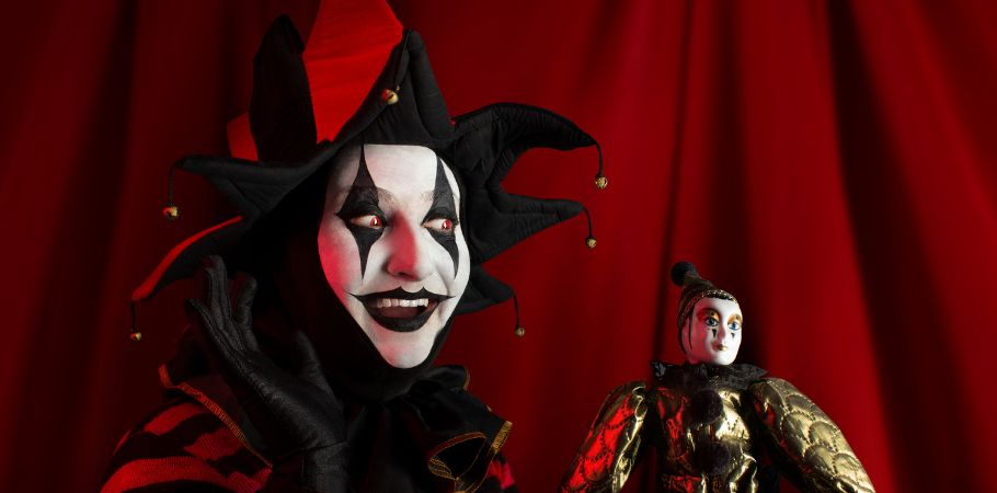 An entertainer in a clown costume, a red nose, and face paint